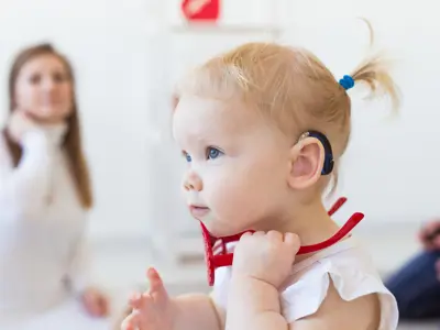 Young girl wearing a hearing aid with caregiver in the background