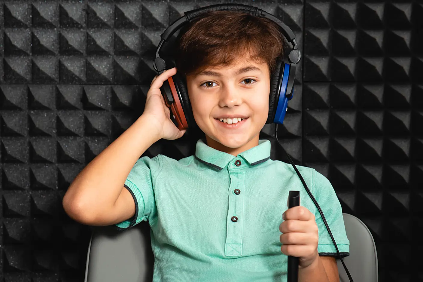 Enfant portant un casque d’écoute et tenant un microphone dans une cabine insonorisée